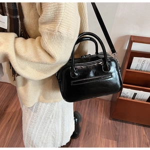 Detail of a black glossy crossbody bag with adjustable strap and twin top handles