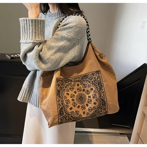 Brown tote bag with mandala print and checkered strap carried by model in home setting