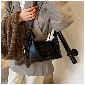 Detail of black leather shoulder bag with ruffled flap and knotted strap detail