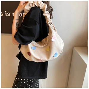 Detail of cream crescent shoulder bag with colorful heart patches and ruffled strap