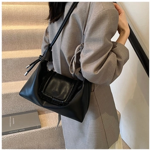 Detail of a black leather shoulder bag with a unique knot strap design on a female model