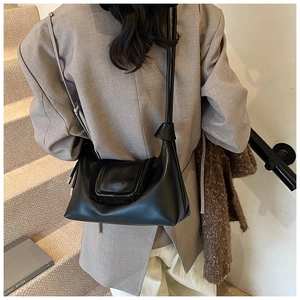 Detail of black crossbody bag with ruffled flap design worn by a model on stairs