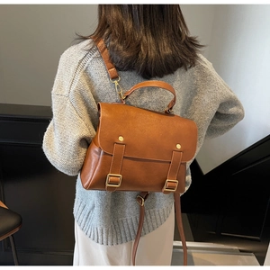Detailed view of caramel leather backpack with vintage metal buckles and handles