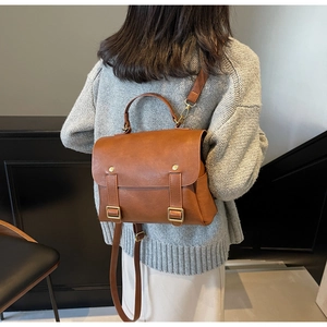 Rear view of woman carrying vintage brown leather backpack with gold buckle details