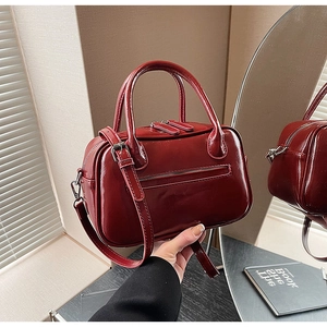 Detail of dark red patent leather handbag featuring glossy finish and metallic zipper