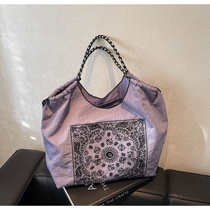 Detailed shot of purple paisley nylon tote bag with braided handles on a black craft book