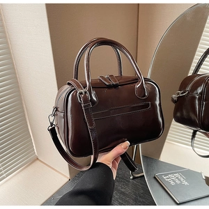 Detailed shot of dark brown glossy leather Boston handbag with adjustable shoulder strap