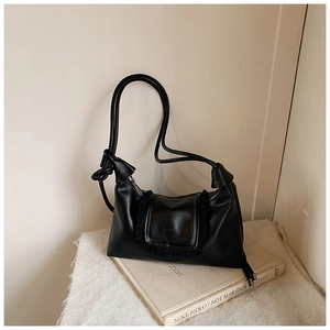 Close-up of black matte leather shoulder bag with ruffled flap on aesthetic books