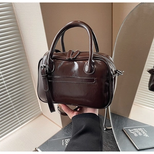 Close-up of a glossy dark brown mini square bag with double zippers and sleek handles