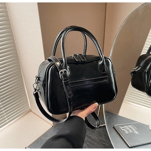 Detail of glossy black leather crossbody bag with silver zippers and dual top handles