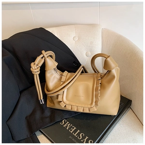 Detail of khaki leather handbag with ruffled edges and knotted handle on dark blazer