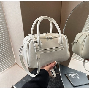 Close-up of white crossbody bag featuring dual zippers and textured faux leather surface