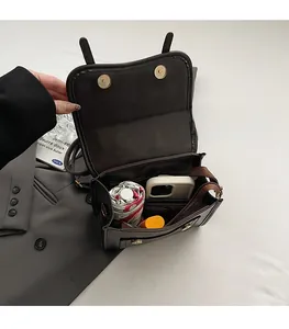 Detail of spacious interior of dark brown leather crossbody bag with items and magnetic buckles