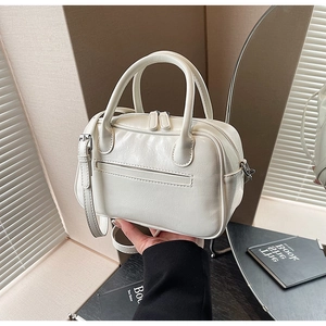 Detail view of the white pleated handbag featuring a top handle and adjustable shoulder strap