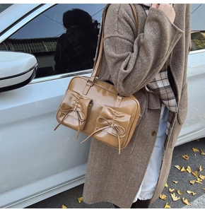 Detail of khaki shiny shoulder bag with decorative bows and front pockets in autumn setting