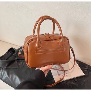 Detail of a brown glossy leather shoulder bag with rounded handles and zipper pocket