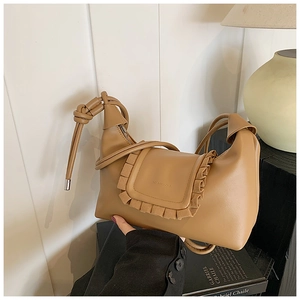 Detail of a brown leather shoulder bag featuring pleated edges and a knotted strap on books