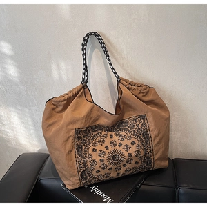 Detailed view of paisley tote bag featuring checkerboard woven strap on leather bench