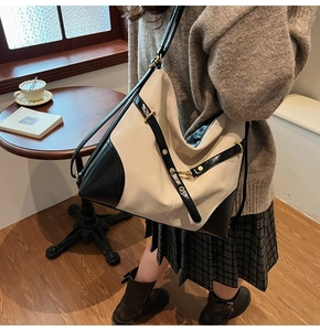 Close-up of beige and black contrast handbag with golden metal buckles in casual setting