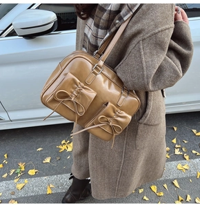 Detail of caramel glossy leather shoulder bag with vintage bow accents on twin front pockets