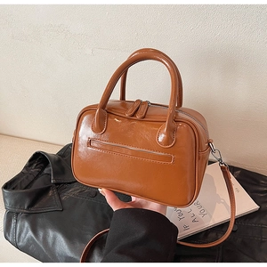 Detail of a brown PU leather crossbody bag with dual zippers and decorative front pocket