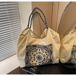 Detail of cream tote bag with black paisley pattern and braided rope handles