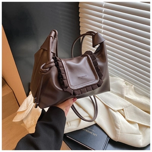 Macro view of dark brown leather handbag featuring ruffle flap and knotted rope strap details