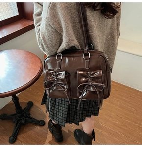Detail of dark brown glossy leather shoulder bag with decorative bow pockets and white stitching