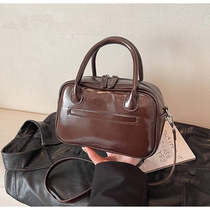Detail of dark brown leather handbag with dual zippers and cylindrical top handle