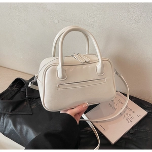 Detail view of cream-white leather handbag with dual zippers and detachable strap