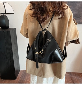 Detail of a black triangular multipurpose bag with gold hardware on a female model