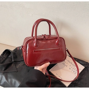 Detail of dark red vintage faux leather handbag with glossy finish and detachable shoulder strap