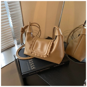 Detailed shot of khaki hobo bag with pleated ruffle flap on a black art book display