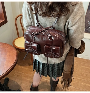 Detail of vintage burgundy leather backpack featuring dual bow-knot pockets and zip closure
