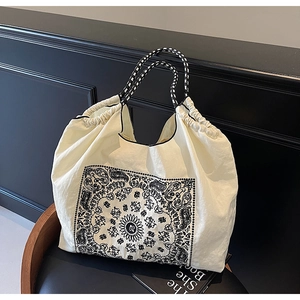 Detail of a beige tote bag with black paisley patterns and braided ropes on a chair