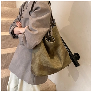 Detail of a large olive canvas tote bag with retro texture shown on a model's shoulder