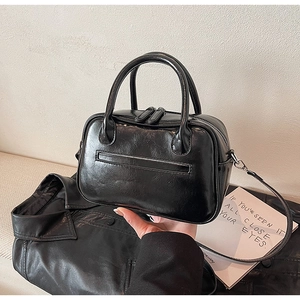 Detail of black glossy handbag featuring double zippers and detachable shoulder strap
