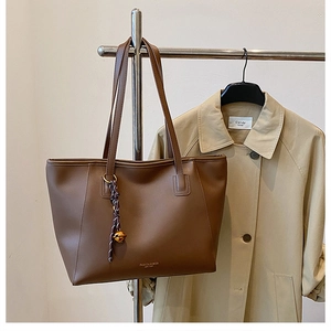 Dettaglio della borsa tote in pelle marrone scuro con scritte oro e ciondolo viola