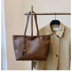 Dettaglio borsa tote in pelle marrone scuro con cinturino intrecciato e campana dorata su trench