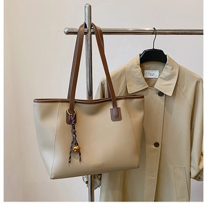 Dettaglio borsa shopper beige con spalline marroni e logo dorato su appendiabiti