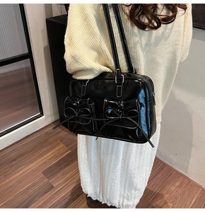 Detail of black glossy shoulder bag with bow pockets and white stitching accents