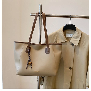 Dettaglio di una grande borsa tote beige con manici marroni appesa accanto a un trench kaki