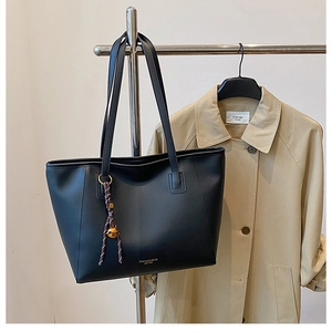 Dettaglio di una grande borsa tote in pelle nera con ciondolo appesa a un trench beige