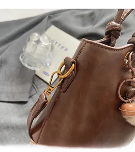 Detail of dark brown leather bucket bag with gold hardware and plush bell charm