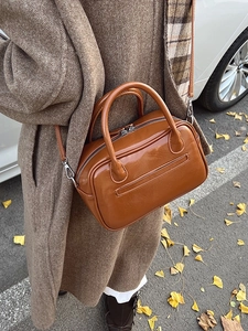 Caramel brown glossy Boston handbag with silver hardware on an autumn street
