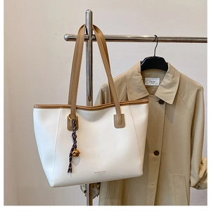 Dettaglio della borsa tote in pelle bianca con manici marroni e ciondolo viola
