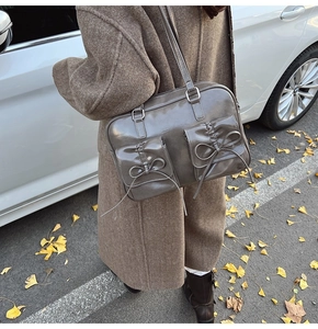 Detail of dark grey patent leather bag featuring double pockets and bow tie accents