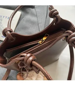 Close-up of brown leather bucket bag with chunky knotted handle and gold metal zipper