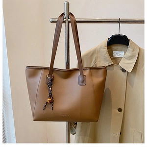 Dettaglio della borsa tote marrone capiente con manici lunghi e ciondolo decorativo