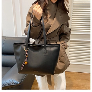 Dettaglio di una grande borsa tote in pelle nera con foulard decorativo e ciondolo
